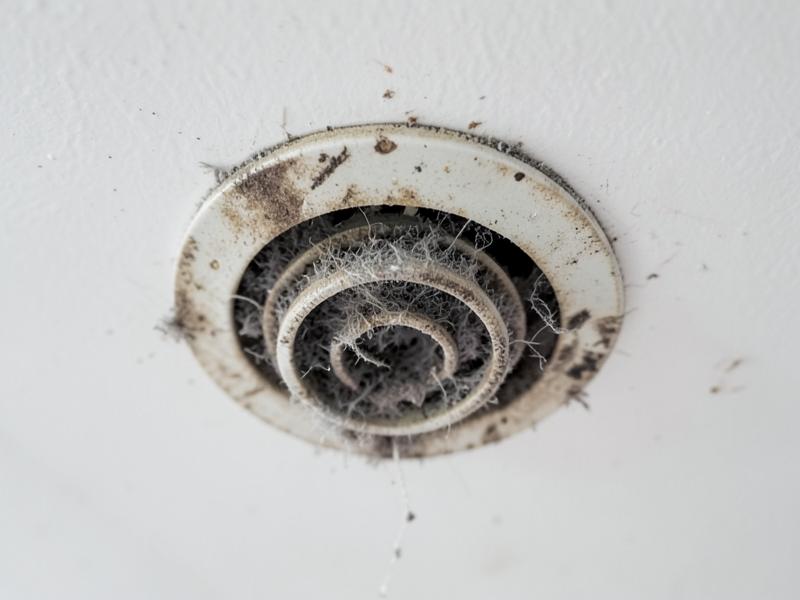 Ceiling air return vent cover clogged with grey dust and lint before a duct cleaning visit